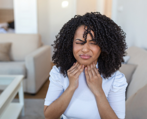 An image of a woman with post nasal drip holding her throat in discomfort.