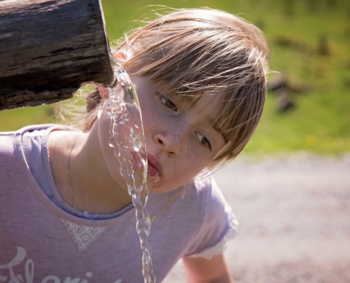 An image of a little girl with dehydration drinking water from a wooden pitcher.