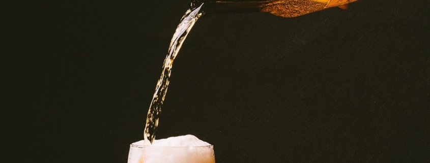 An image of a hand pouring beer into a glass to limit alcohol intake.