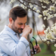 An image of a man with seasonal allergies wiping his nose beside a flowing plant.