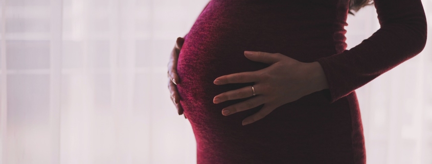 An image of the torso of a pregnant woman wearing a dress.